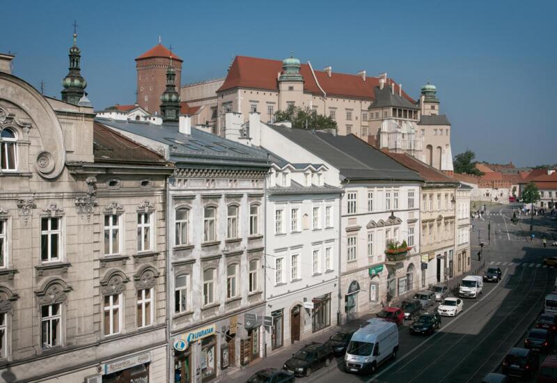 Historyczna ulica w centrum z ozdobnymi fasadami, sklepami i restauracjami na parterze, torami tramwajowymi i widokiem na zamek.