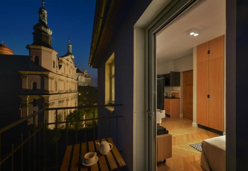 Balkon nocą z zestawem do herbaty, nowoczesny apartament z parkietem i aneksem kuchennym, z widokiem na podświetloną zabytkową fasadę kościoła