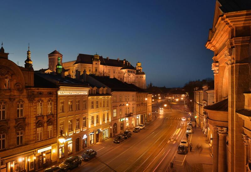 Urokliwa ulica w zabytkowym centrum o zmierzchu, podświetlone witryny, zaparkowane auta i zamek na wzgórzu