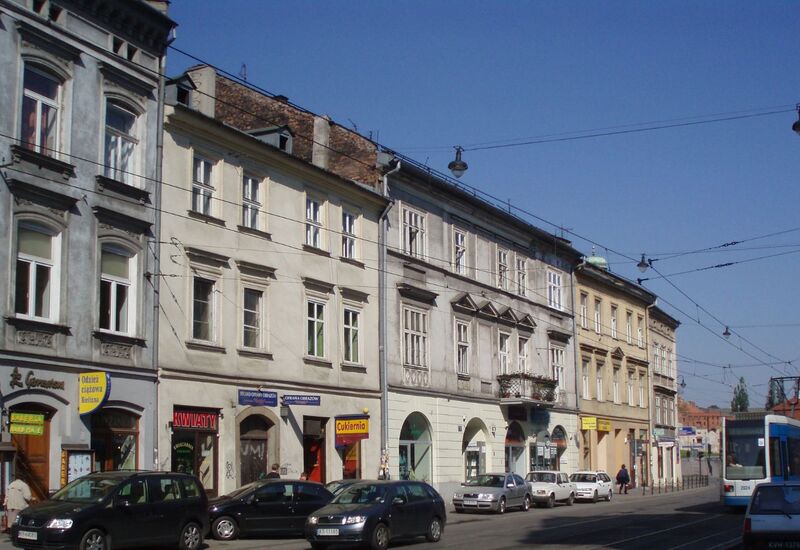 Historyczne trzypiętrowe elewacje z lokalami na parterze, zaparkowanymi samochodami i tramwajem na słonecznej ulicy