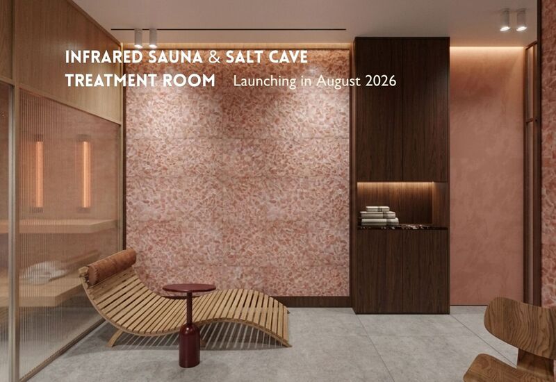 Strefa relaksu z łukowatą drewnianą leżanką, różową ścianą z soli, przeszkloną sauną na podczerwień i ręcznikami w szafce.