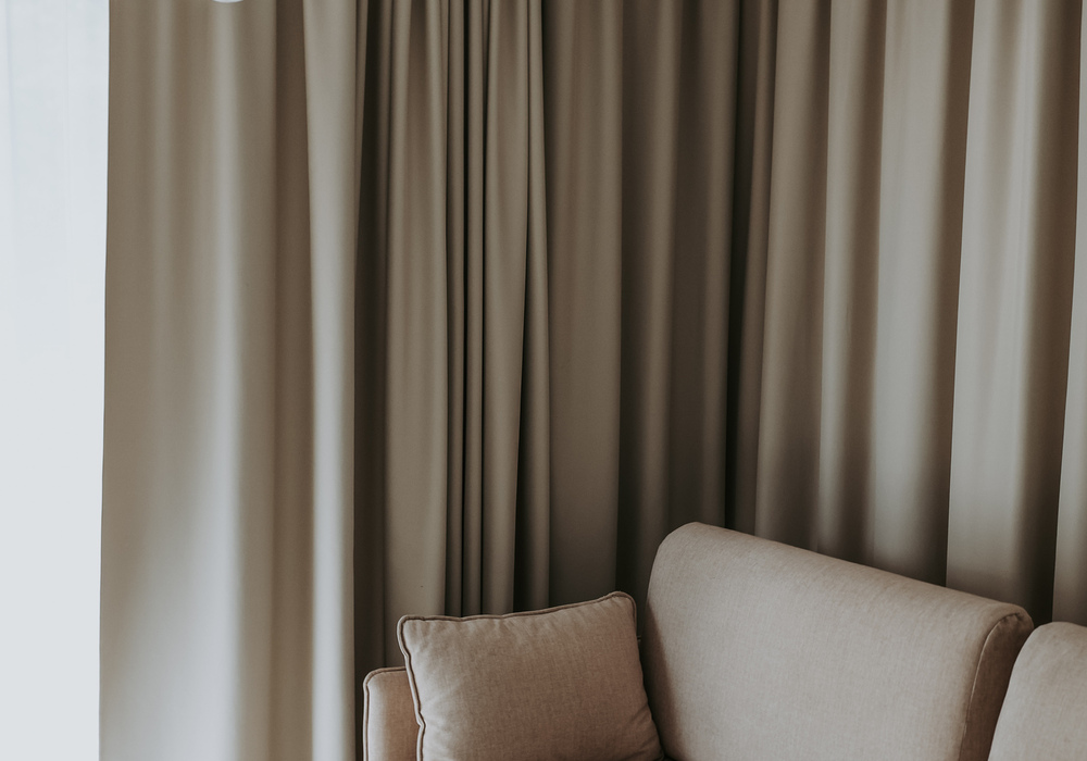 Cozy hotel lounge corner with beige sofa, plump cushion, floor-to-ceiling curtains and modern pendant light