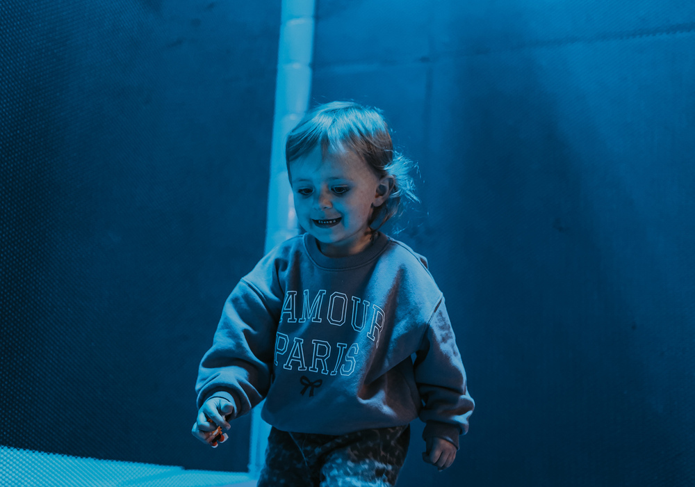 Toddler jumping on padded indoor trampoline in family play area with soft blue lighting