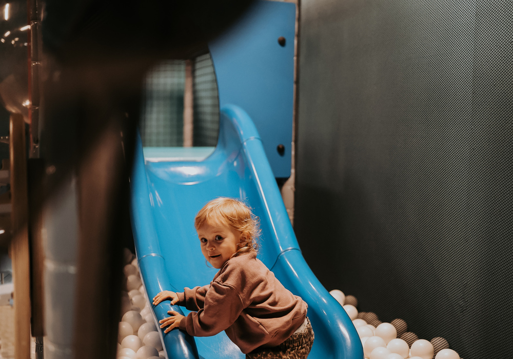 Toddler climbing a blue slide into a white ball pit in the hotel's indoor kids play area