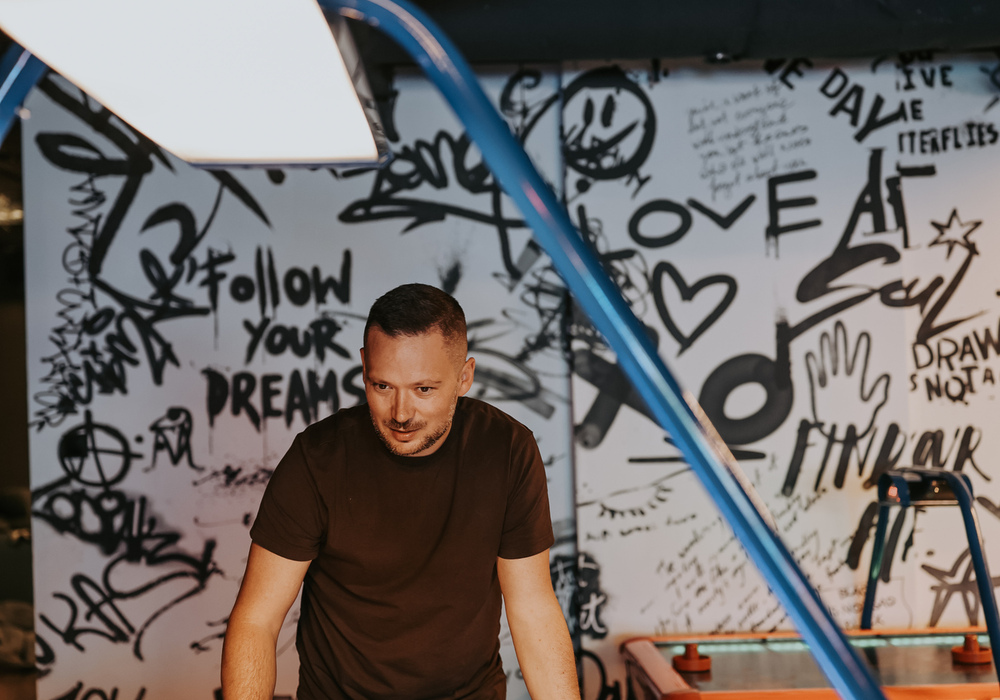Man playing air hockey at a neon-lit arcade table in a hotel game room with graffiti mural and relaxed, family-friendly vibe