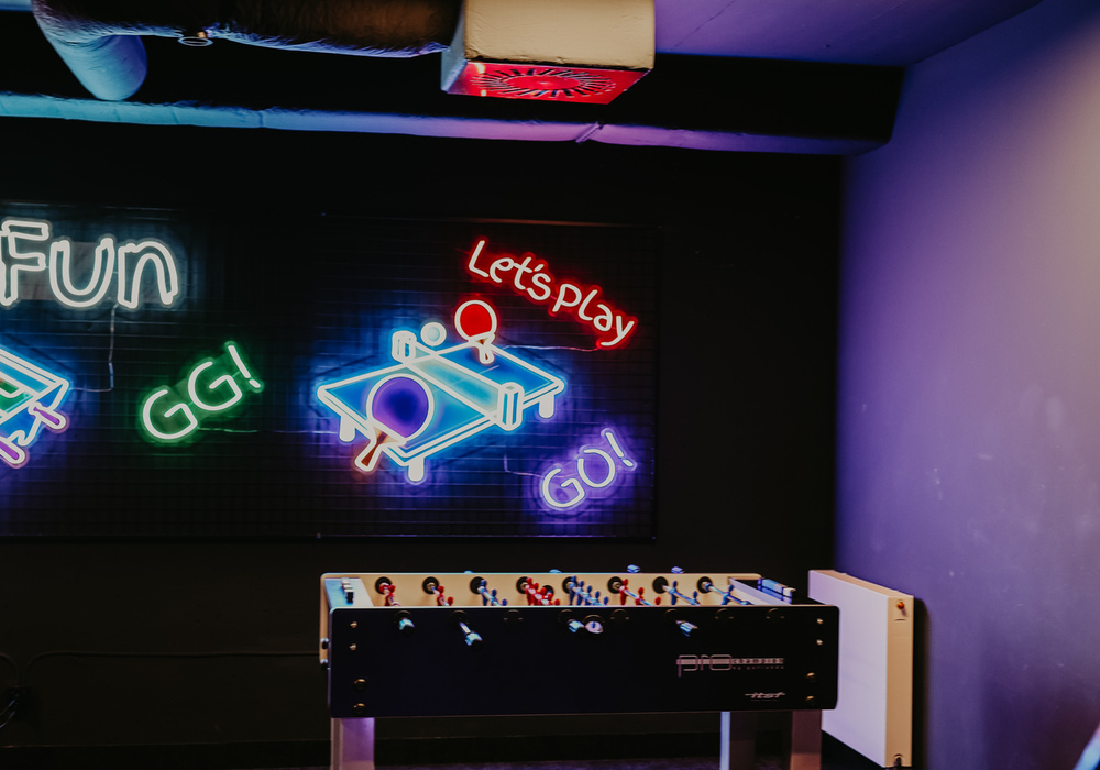 Hotel game lounge with foosball table, neon 'Let's Play' sign and colorful mood lighting