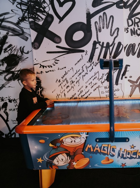 Children playing air hockey at a colorful 'Magic Hockey' table against a graffiti mural in a hotel family game room