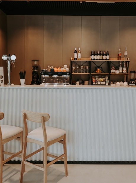 Modern hotel coffee bar with espresso machine, beer taps, wine and spirits on shelves, two wooden bar stools