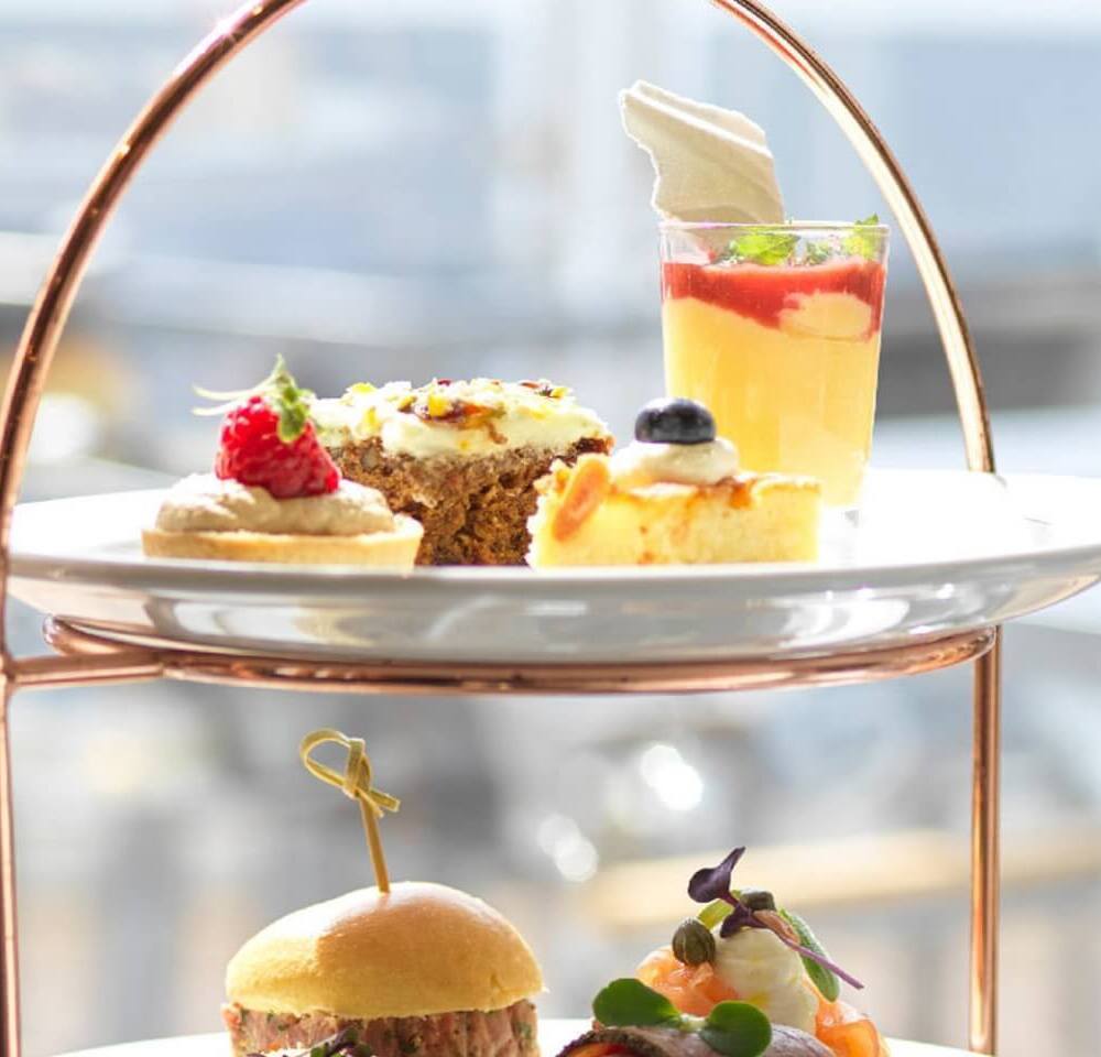 Three-tier copper stand with pastries (cake, tart, layered mousse) and savory bites: mini slider and smoked salmon canapé