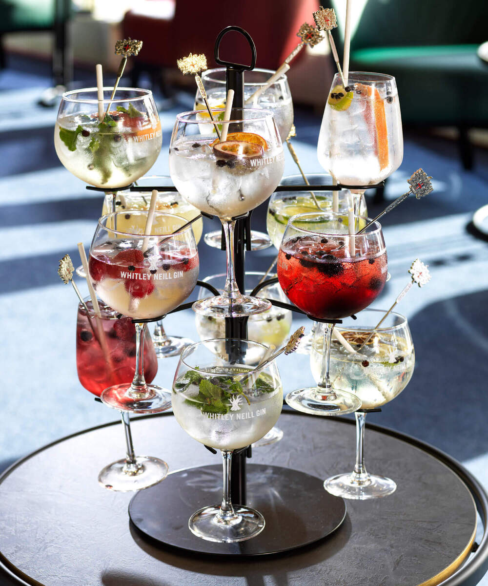 Tiered tower of ice-filled gin balloon glasses with fruit, berries and mint garnishes served on a hotel lounge table.