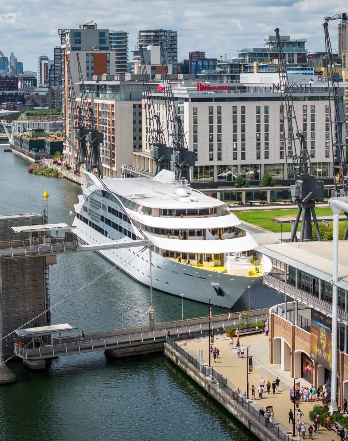 Waterfront hotel by the marina with large white cruise yacht, historic dock cranes, lively promenade and city skyline views