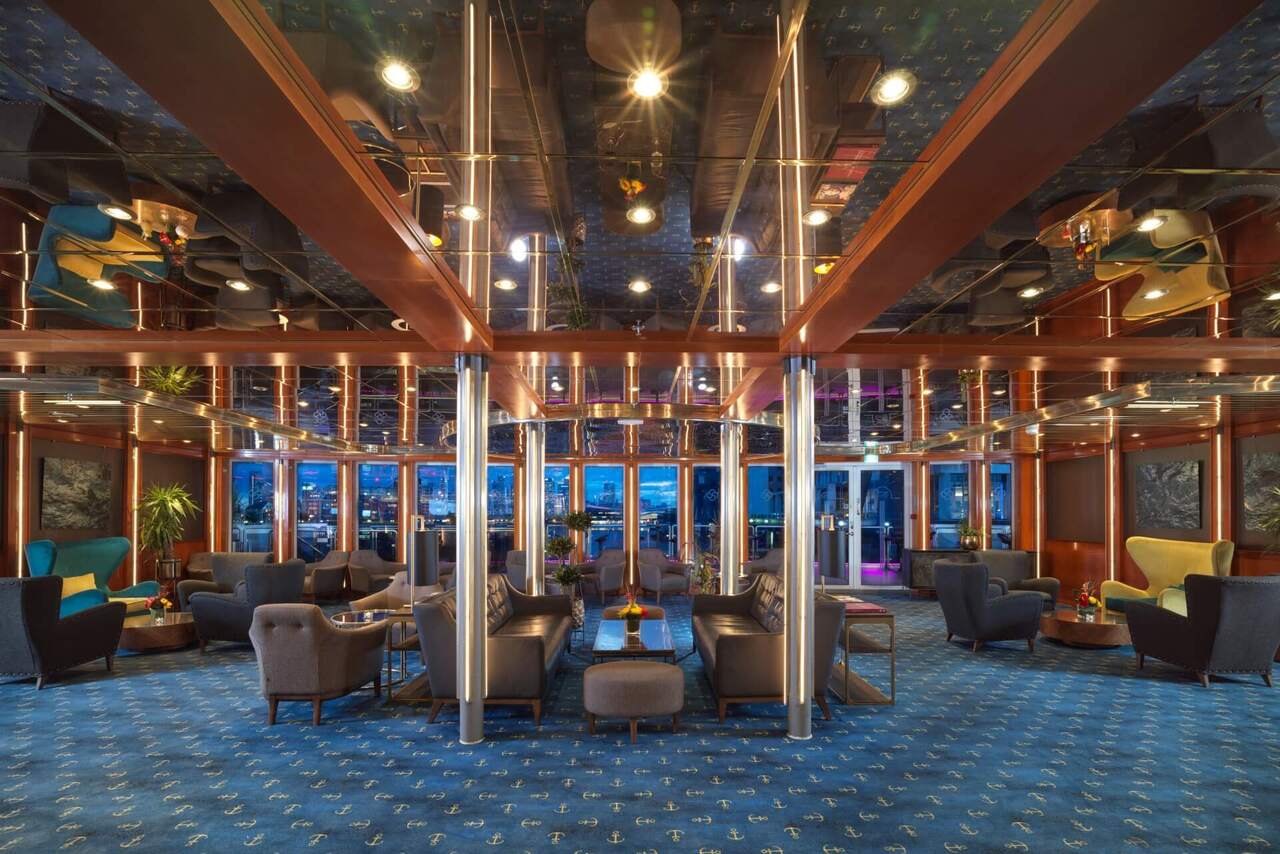Nautical lounge with mirrored ceiling, anchor-pattern blue carpet, leather sofas and armchairs, illuminated metal columns and waterfront views