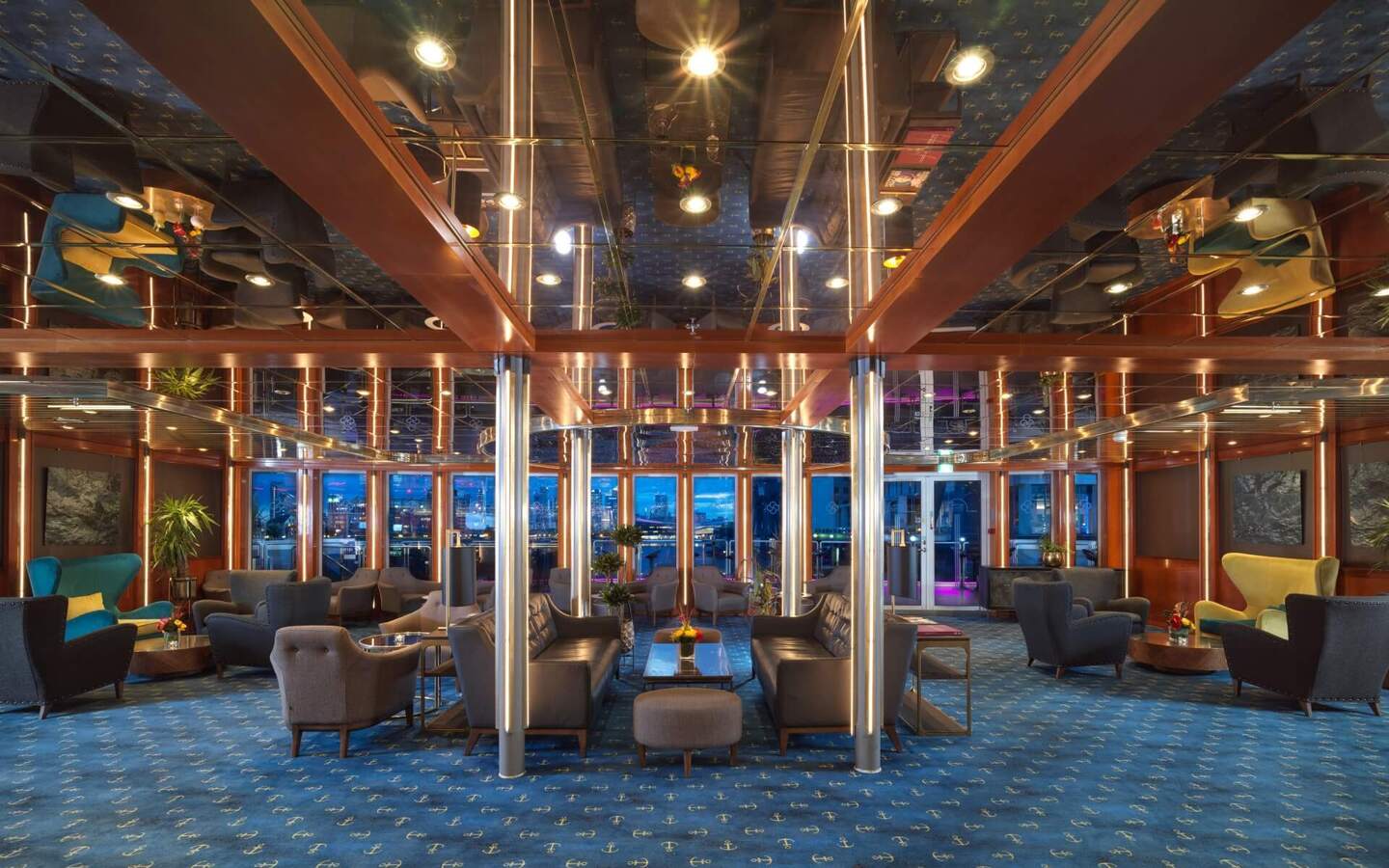 Nautical lounge with mirrored ceiling, anchor-pattern blue carpet, leather sofas and armchairs, illuminated metal columns and waterfront views