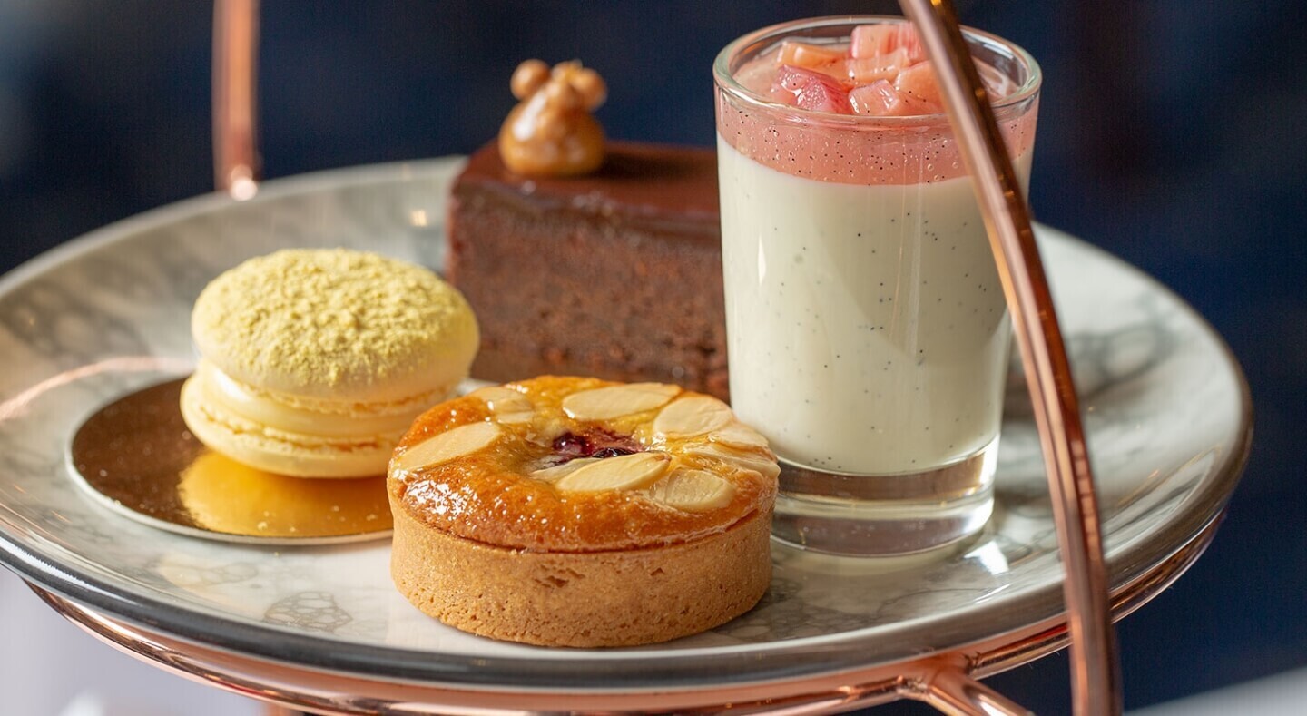 Afternoon-tea plate: vanilla panna cotta with fruit compote, almond tart, lemon macaron and chocolate cake on marble tier