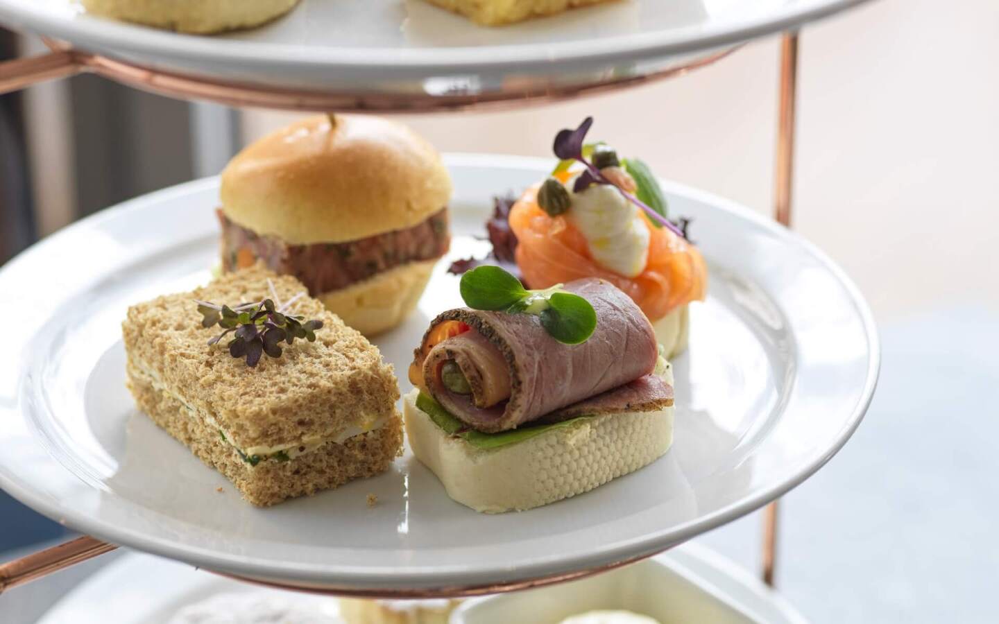 Tiered afternoon-tea stand with assorted finger sandwiches and canapés: roast-beef roll, smoked salmon canapé, mini slider.
