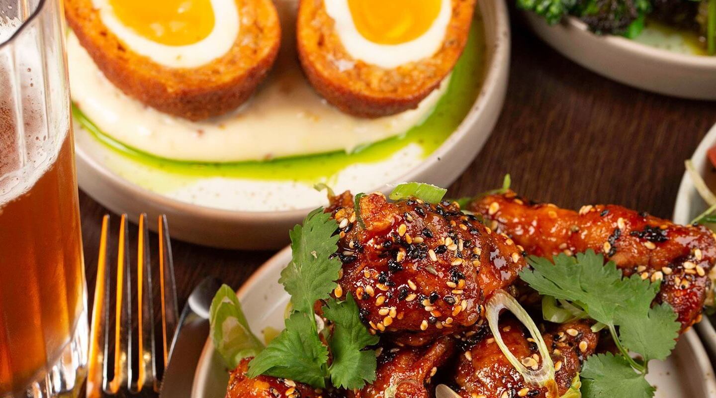 Sesame-glazed chicken wings garnished with cilantro, halved Scotch eggs on creamy puree, salad and a pint of beer