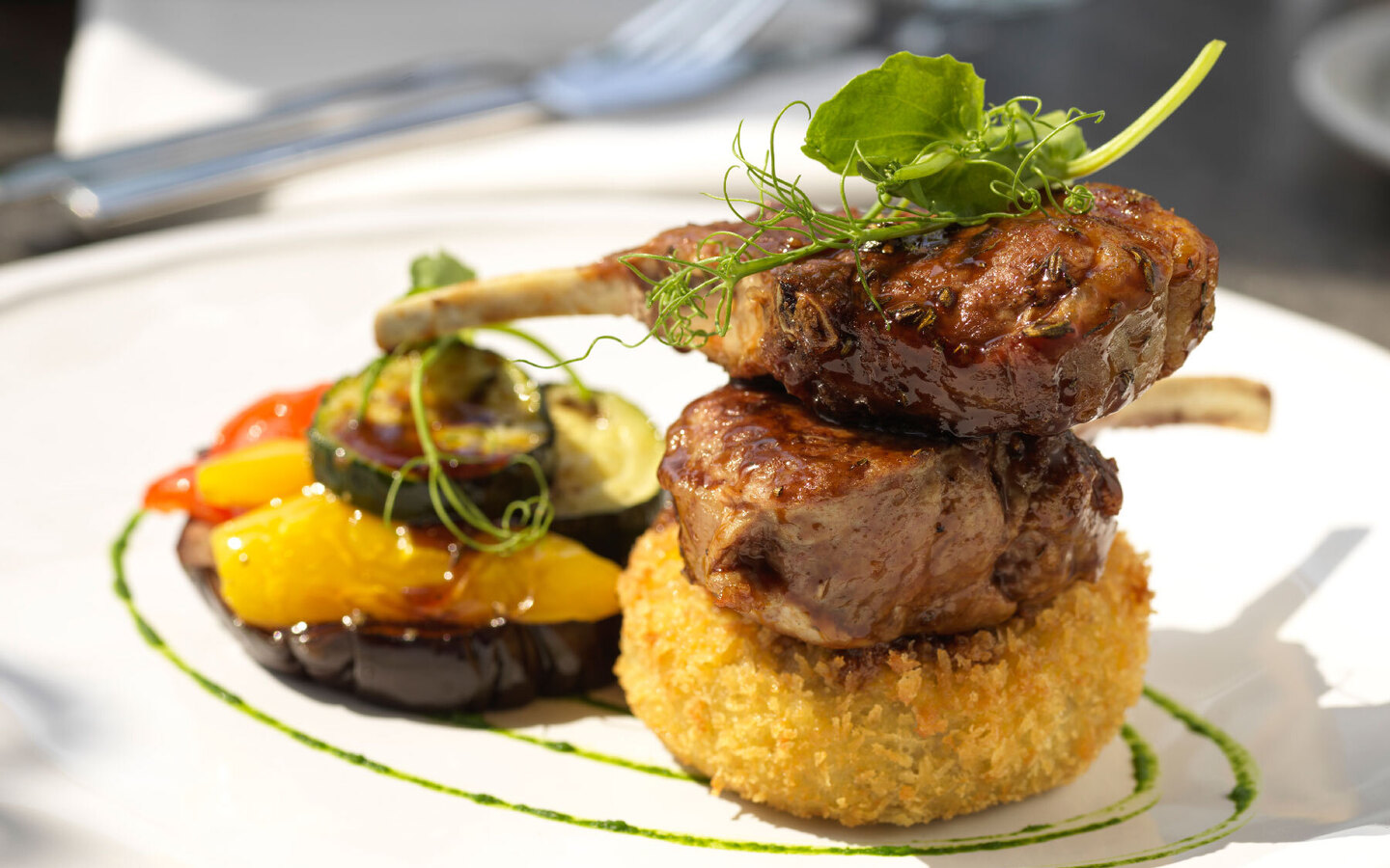Glazed lamb chops stacked on a golden croquette, topped with pea shoots, with roasted zucchini, peppers and herb sauce.