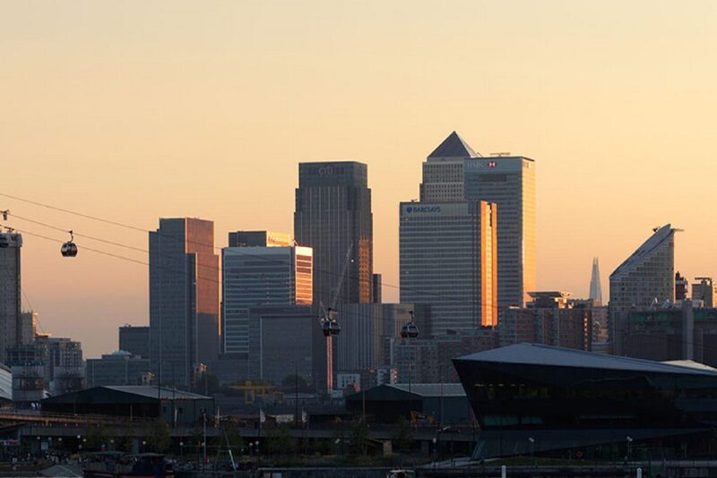 Sunset view of Canary Wharf skyline and the O2 dome from the riverfront, with Emirates cable cars crossing above.