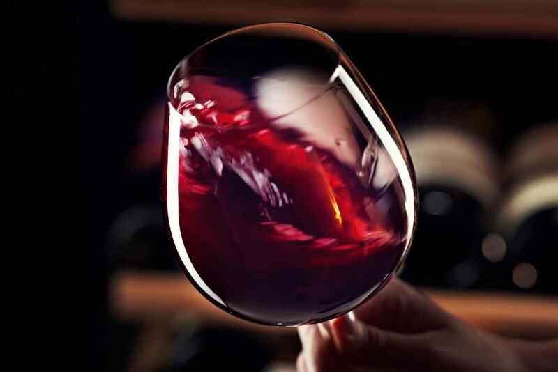 Hand swirling ruby red wine in a crystal glass, close-up in an upscale hotel restaurant or wine cellar.