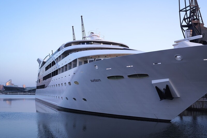 Sunborn superyacht docked at a calm marina at dusk, multi-deck guest balconies, waterfront promenade and city skyline views.