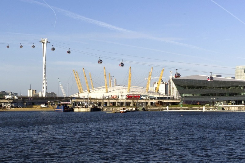Riverfront view of glass waterfront and apartments, Emirates cable cars over the water with O2 dome and city skyline.