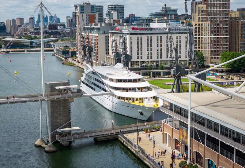 Waterfront hotel by the marina with large white cruise yacht, historic dock cranes, lively promenade and city skyline views