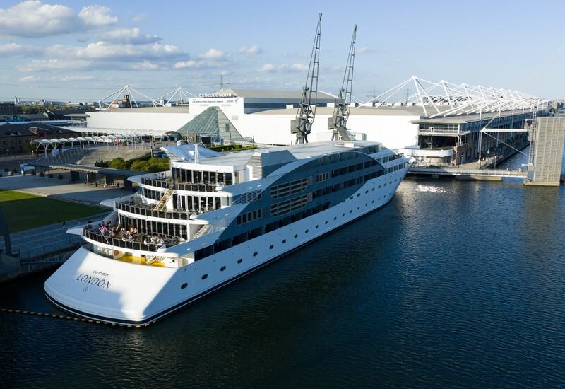 Luxury Sunborn London floating hotel docked at ExCeL London, multi-deck terraces with guests dining and waterfront views.