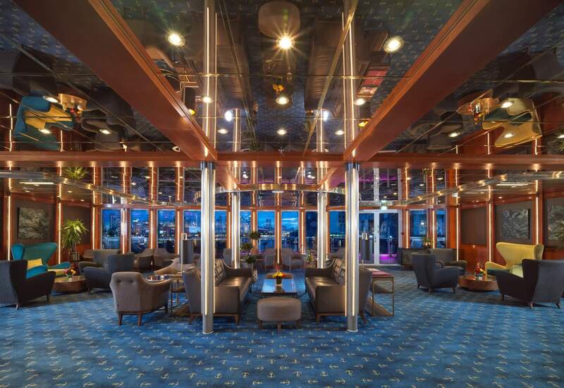 Nautical lounge with mirrored ceiling, anchor-pattern blue carpet, leather sofas and armchairs, illuminated metal columns and waterfront views