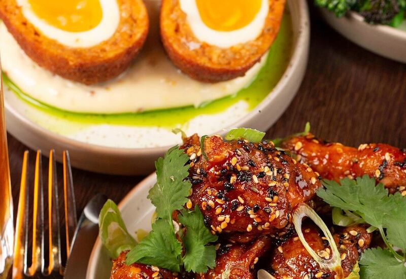 Sesame-glazed chicken wings garnished with cilantro, halved Scotch eggs on creamy puree, salad and a pint of beer