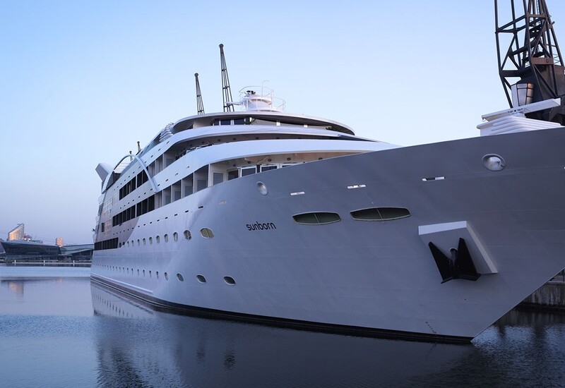Sunborn superyacht docked at a calm marina at dusk, multi-deck guest balconies, waterfront promenade and city skyline views.
