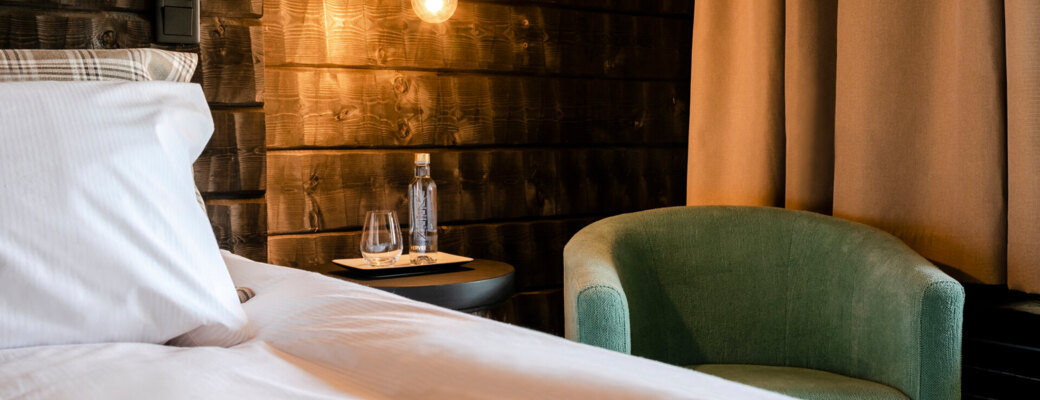 A single light bulb illuminating a bed, a small sofa and a nightstand with warm light.