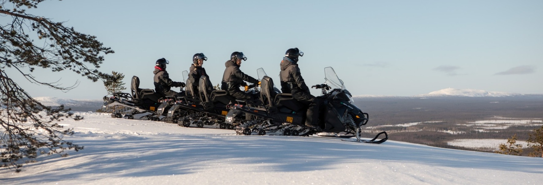 A line of people on snow electro mobiles getting ready to ride downhill.