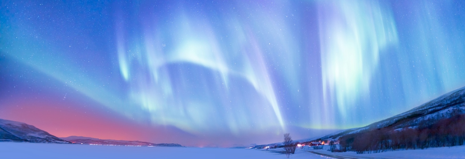 Northern lights above a frozen lake, with a small village on its right bank.