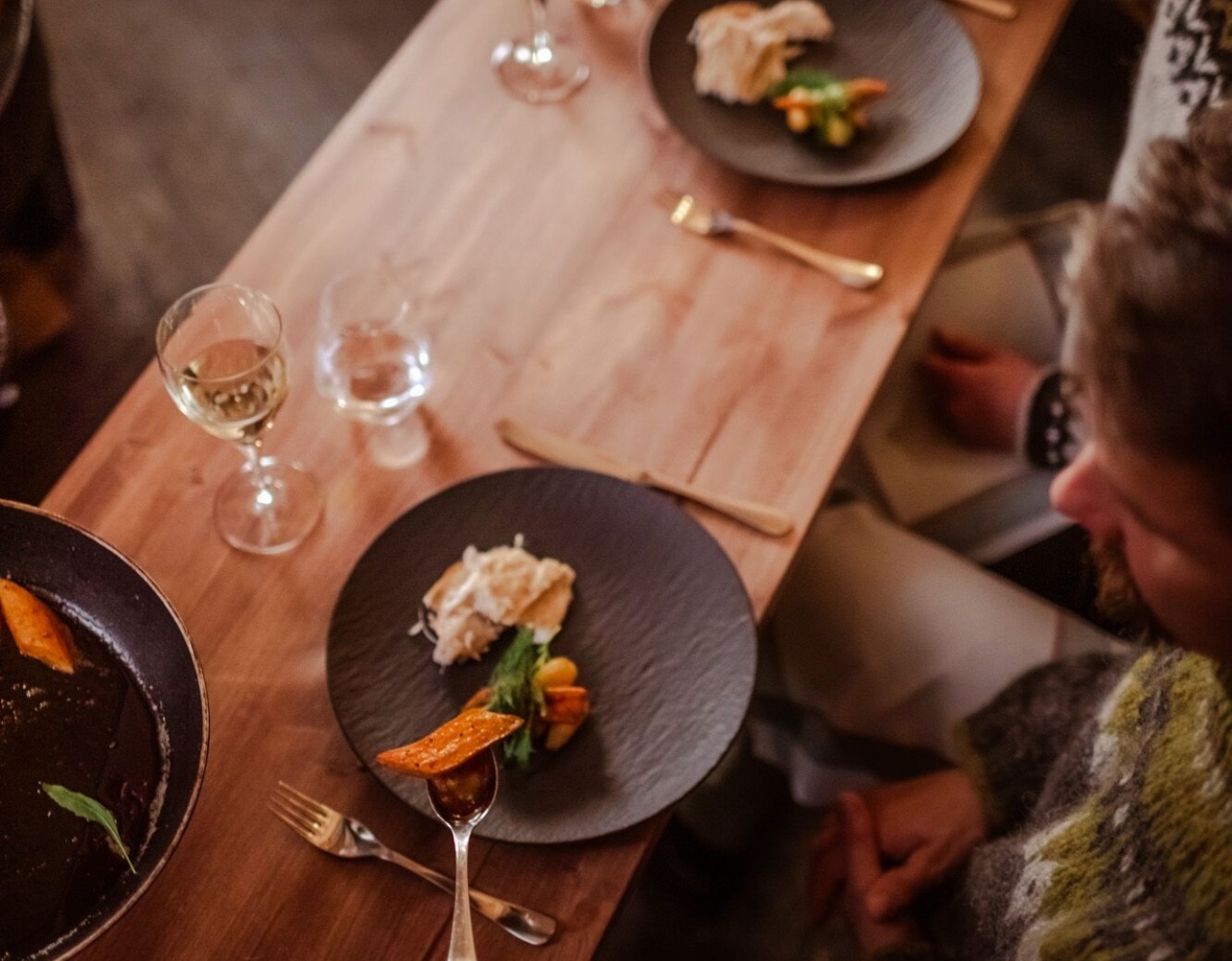Table en bois chaleureuse dans un restaurant, deux assiettes avec légumes modernes et verre de vin rouge pour convives.