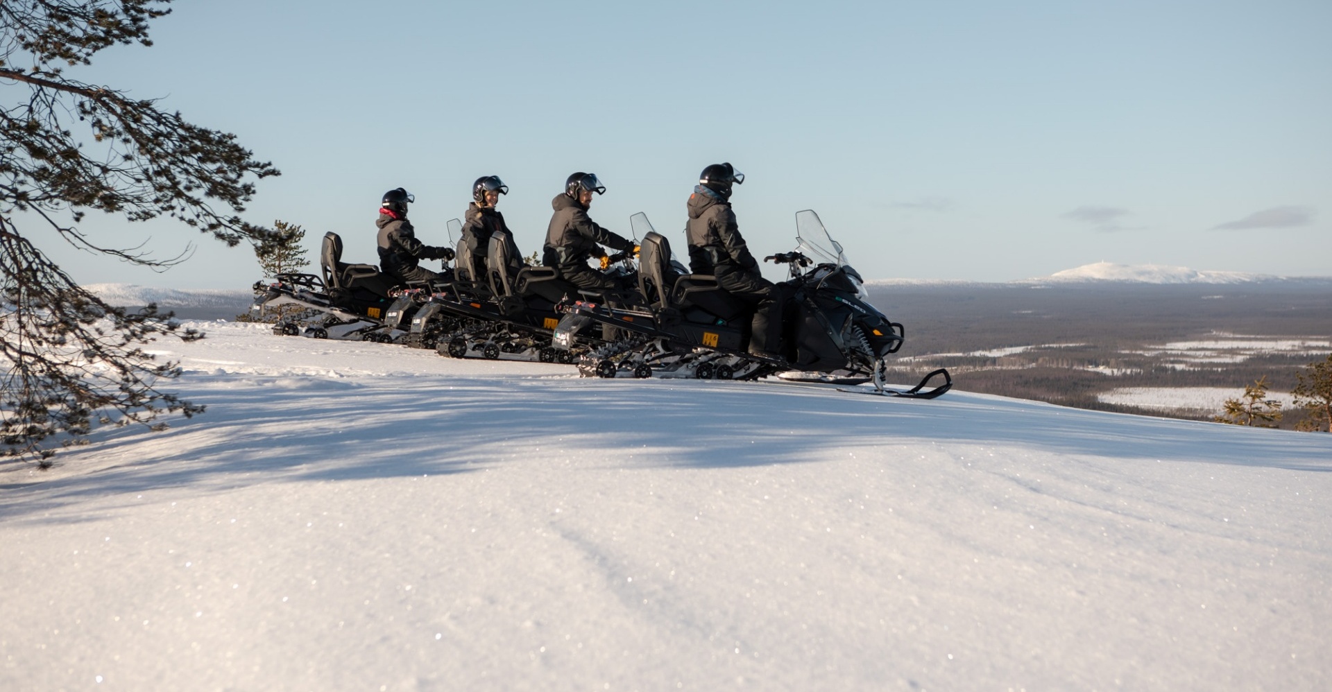 A line of people on snow electro mobiles getting ready to ride downhill.