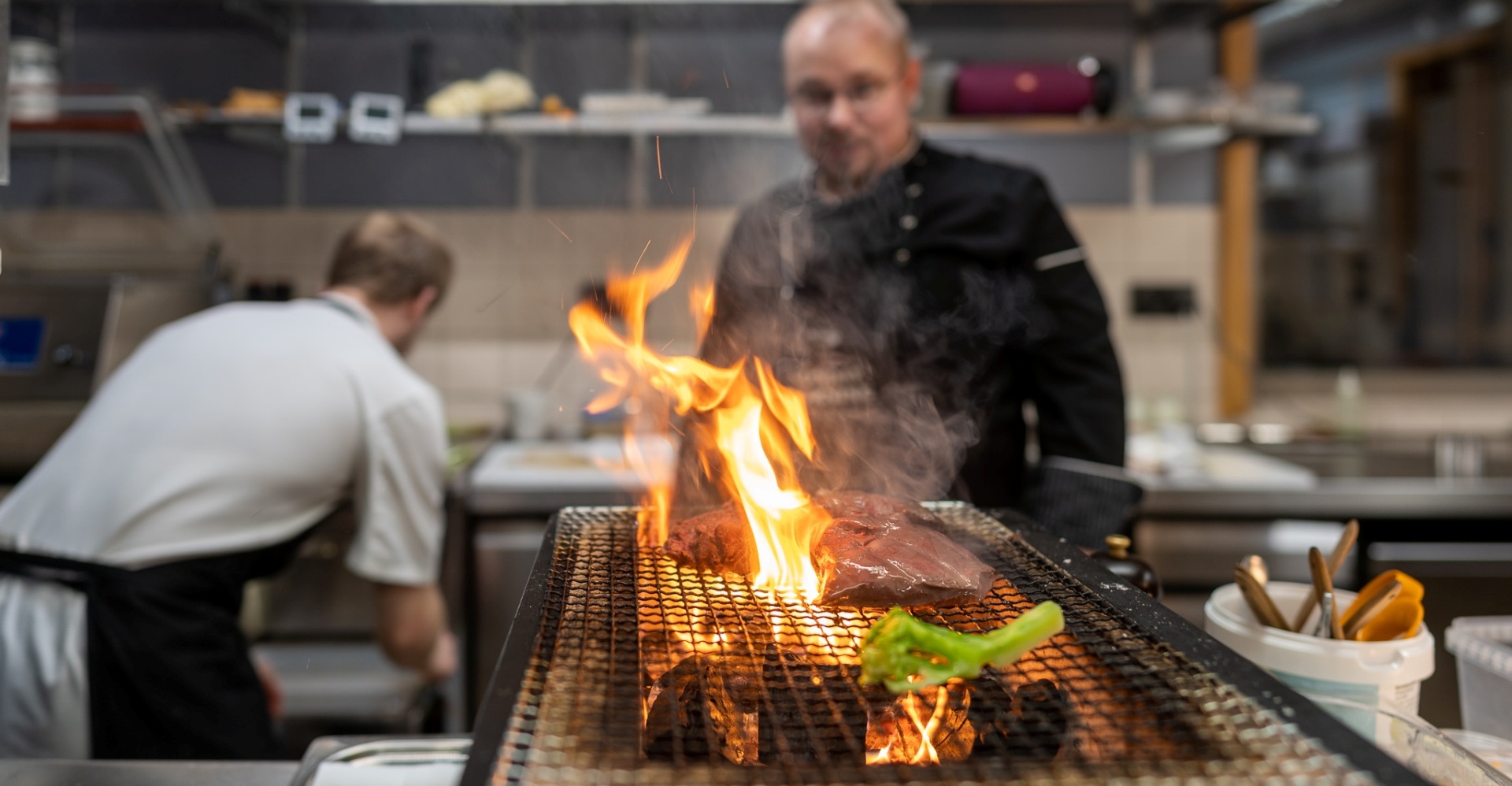 The chef roasting meat on a grill fireplace in the kitchen.