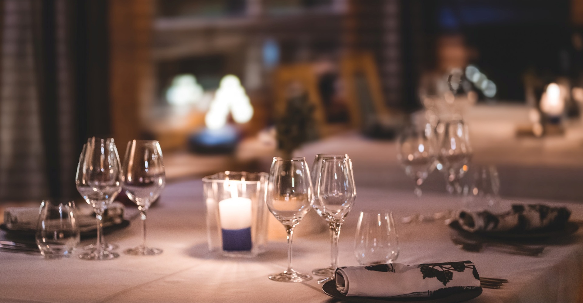 Wine glasses standing on an elegant tablecloth, next to a lit candle.