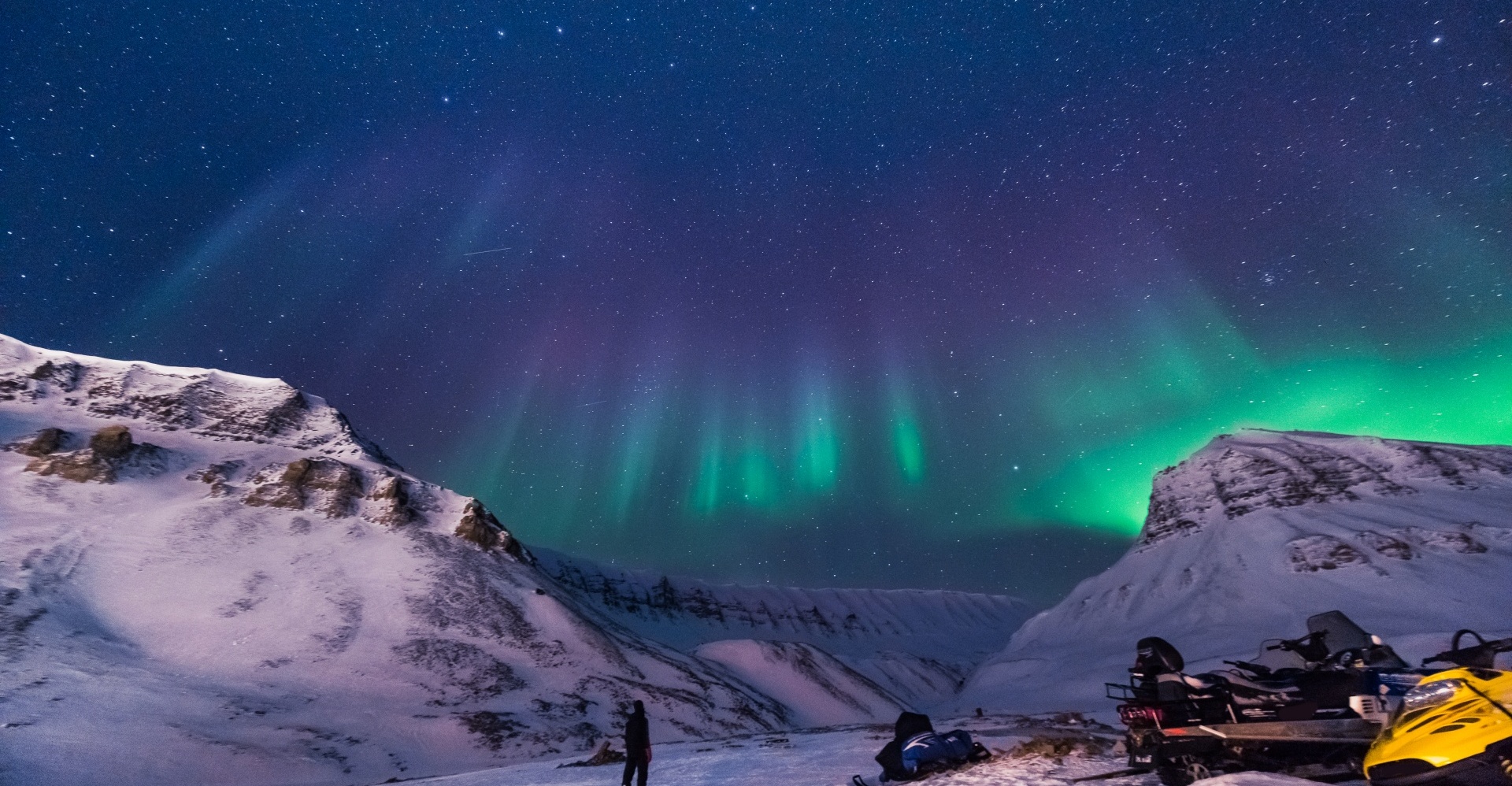 Northern lights in a valley, turning from blue, through purple to green as they descend.