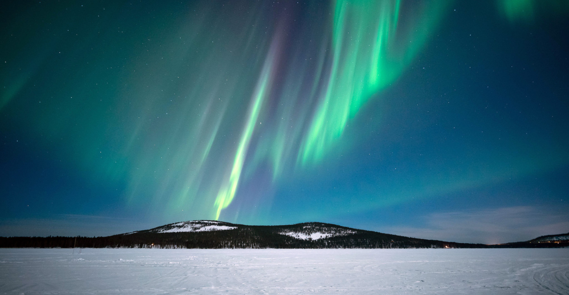 Green northern lights falling onto a hill in the distance.