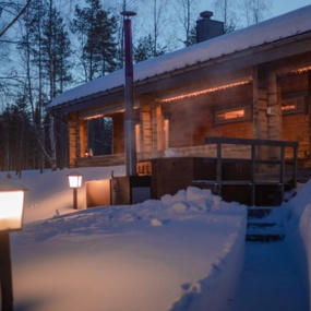 A cozy wooden lodge nestled in the snow in the evening, illuminated by warm light.