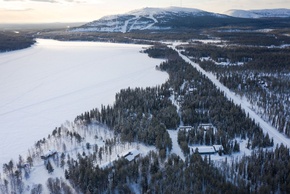 Paysage enneigé avec chalets en forêt près d’un lac gelé et une montagne boisée en arrière-plan
