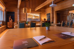 Sala de reuniones rústica en lodge con gran mesa de madera, blocs 'Room for Ideas', proyector, sillas y luz natural
