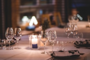 Wine glasses standing on an elegant tablecloth, next to a lit candle.