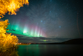 Vibrant northern lights over a tranquil lake with autumn trees glowing gold under a starry night sky