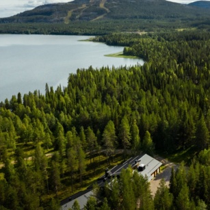 Summer Lapland a lake surrounded by bright-green trees, amongst which sits the Sunday Morning Resort