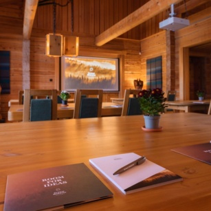 A laptop and a notepad lying on a wooden table in a timber conference room.