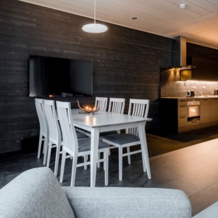 A table with 3 chairs on each sides standing in front of a TV. A cozy kitchen in the background.
