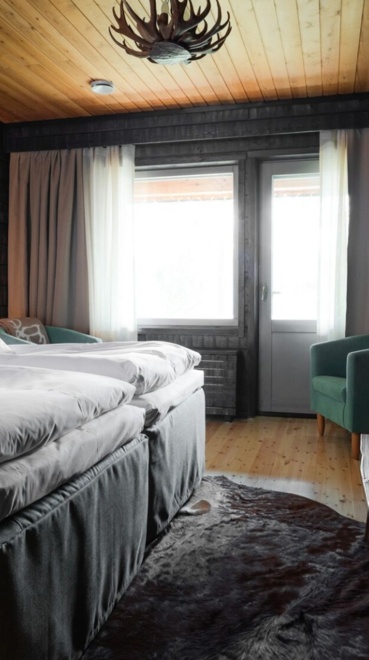 A wooden lodge bedroom with 2 single beds, a bearskin rug and a stone TV stand.