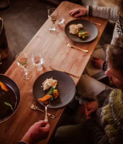Gourmet dishes served on black, textured plates along with a glass of white wine.