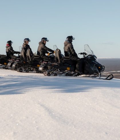 A line of people on snow electro mobiles getting ready to ride downhill.